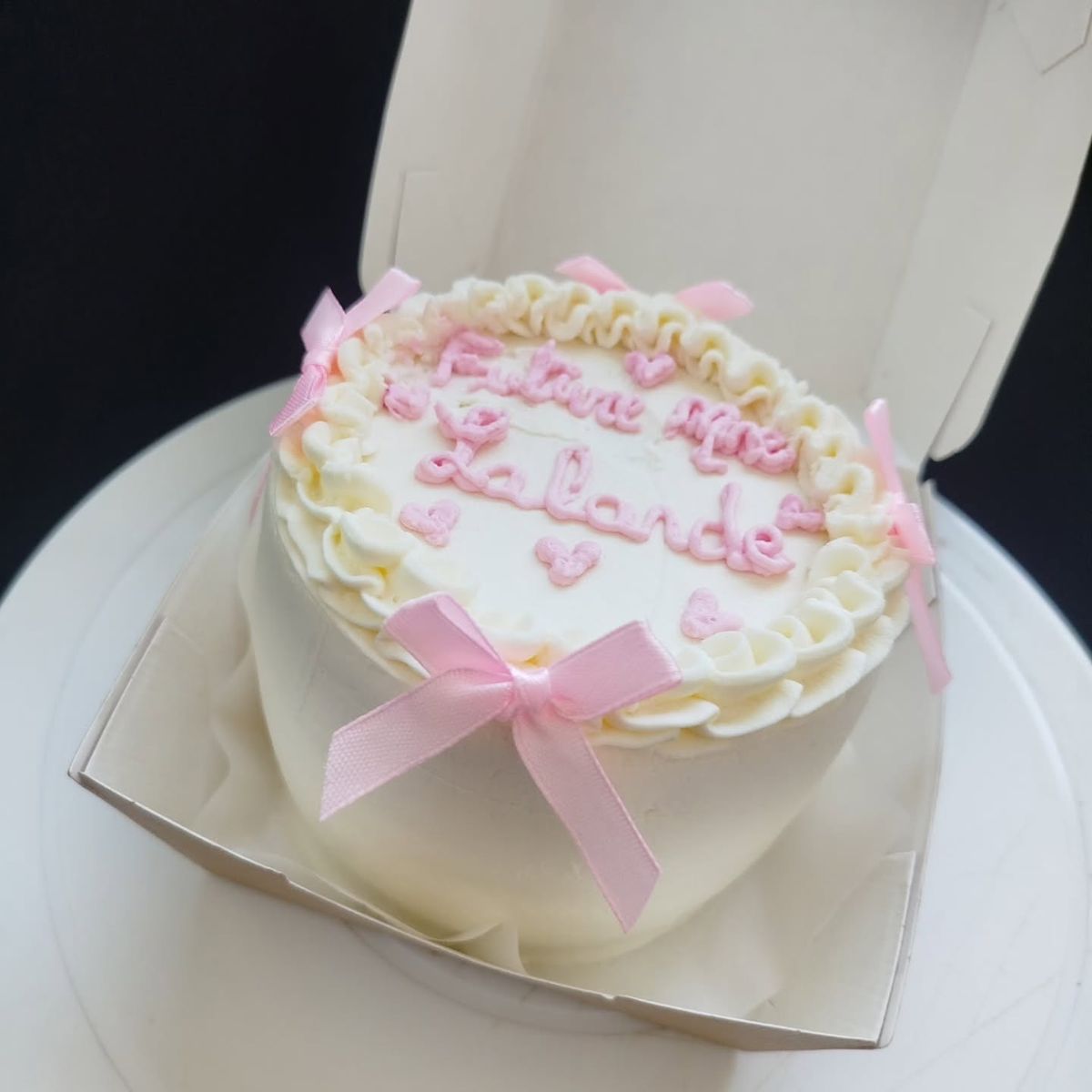 Bento cake blanc décoré de nœuds roses et d'un message écrit à la poche