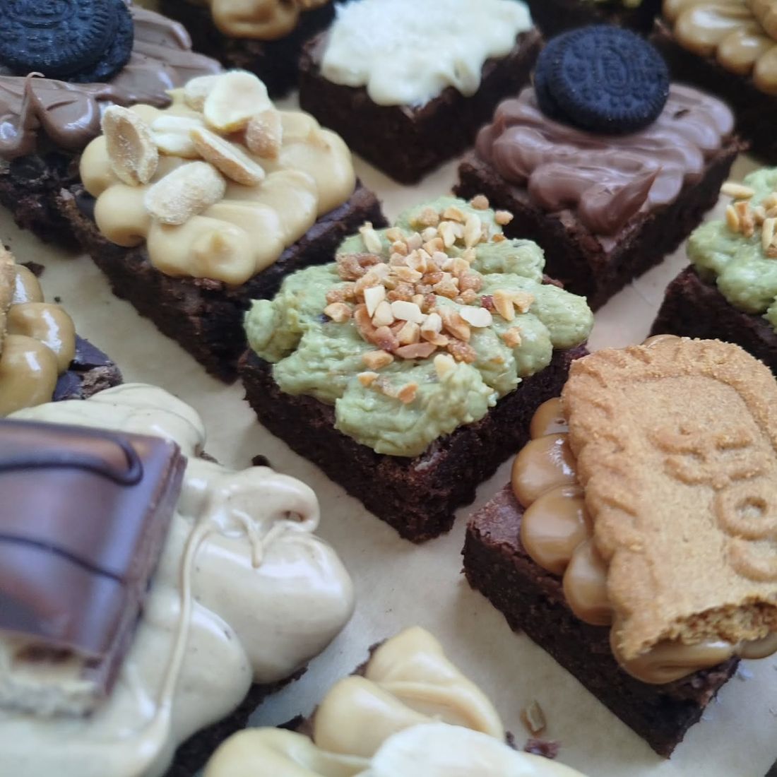 Gros plan sur des brownies garnis de crème pistache, cacahuètes et spéculoos