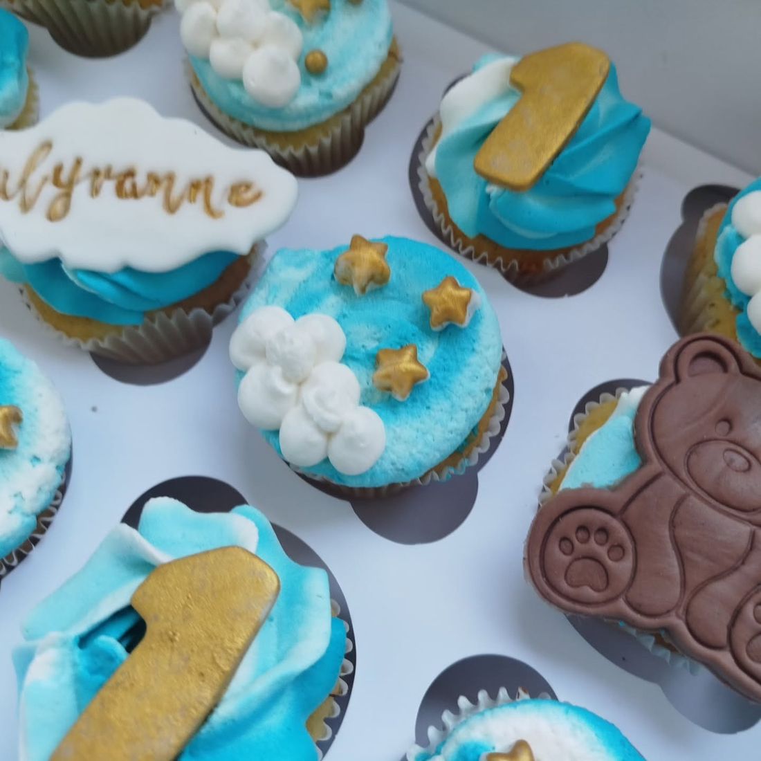 Gros plan sur des cupcakes bleus avec nuages de crème, étoiles dorées et ourson en chocolat