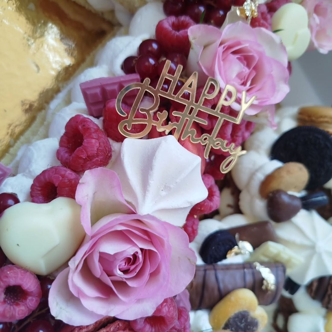 Gros plan sur un number cake : roses, framboises, meringue et topper Happy Birthday doré